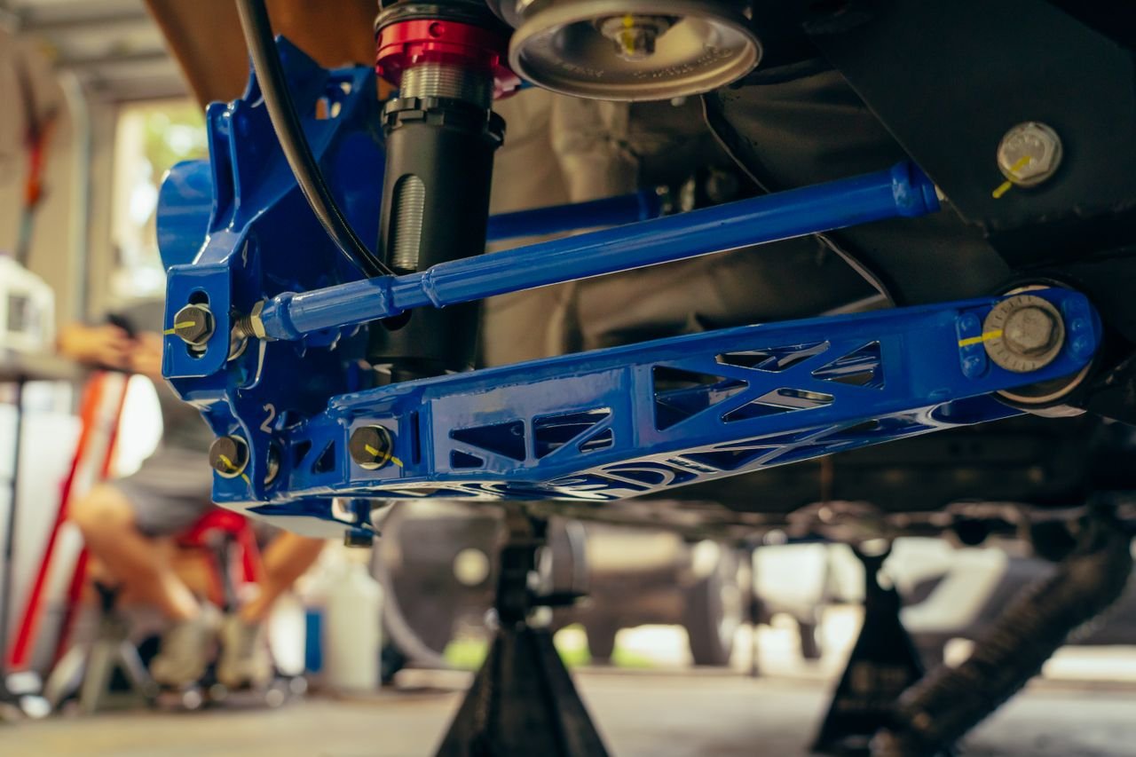 Blue performance control arm and coilover fitted to a vehicle on the lift